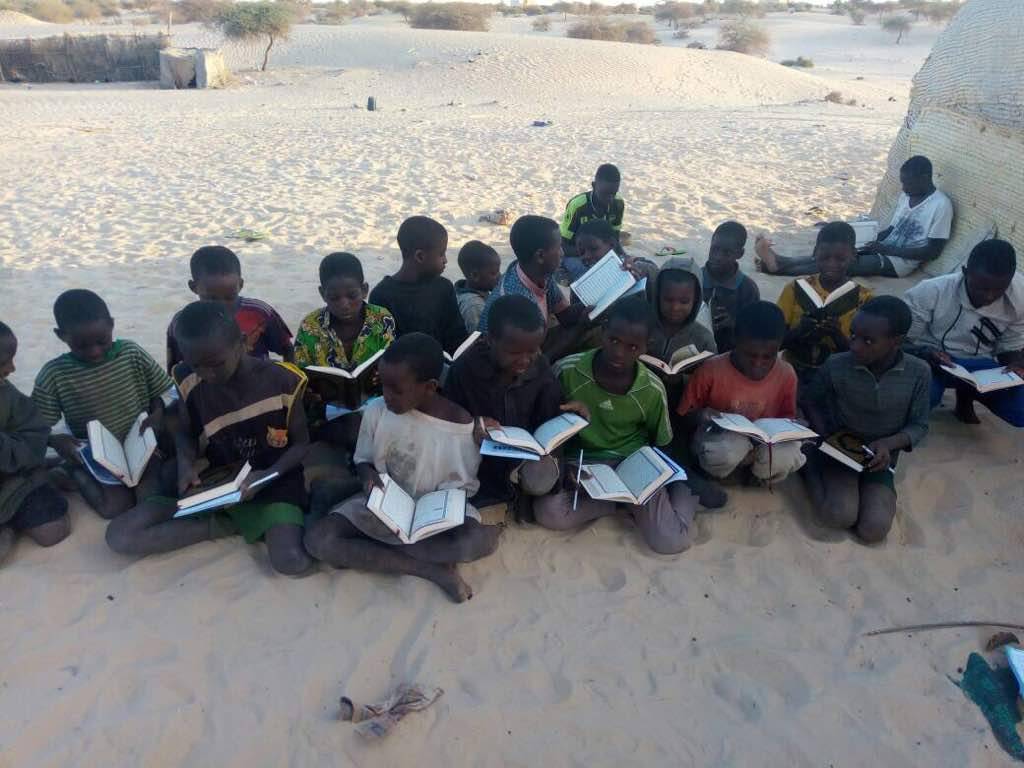 Des enfants assis dans le sable lisent les livres qu'ils viennent de recevoir.